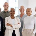 Grupo diversificado de pessoas calvas em um ambiente de escritório, sorrindo e interagindo amigavelmente.