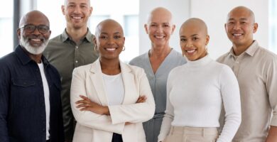 Grupo diversificado de pessoas calvas em um ambiente de escritório, sorrindo e interagindo amigavelmente.